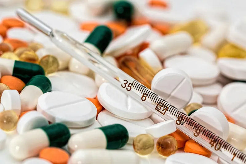 Medicamentos en tabletas y cápsulas junto a un termómetro